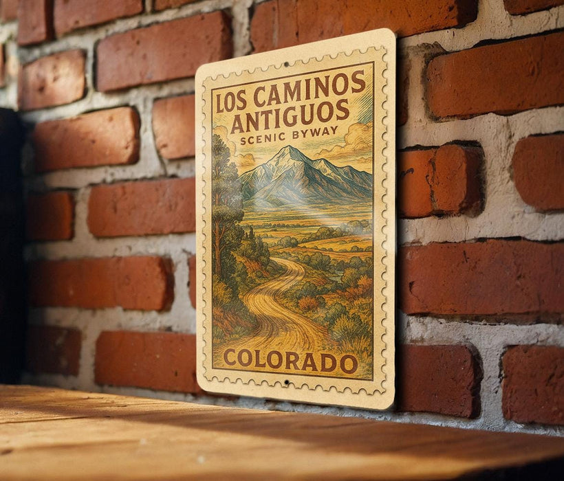 A vintage-style metal sign with a mountain landscape and road, mounted on a brick wall.