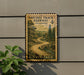 A vintage postage stamp depicting a winding road through a forest, mounted on a wall next to a plant.