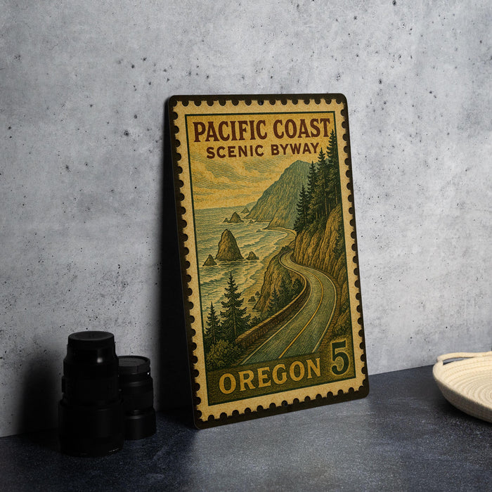 A vintage-style metal sign with a scenic coastal landscape, featuring a winding road and mountains in the background, is displayed on a gray countertop.