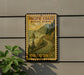 A vintage-style metal sign with a scenic coastal landscape, mounted on a wall next to a plant.