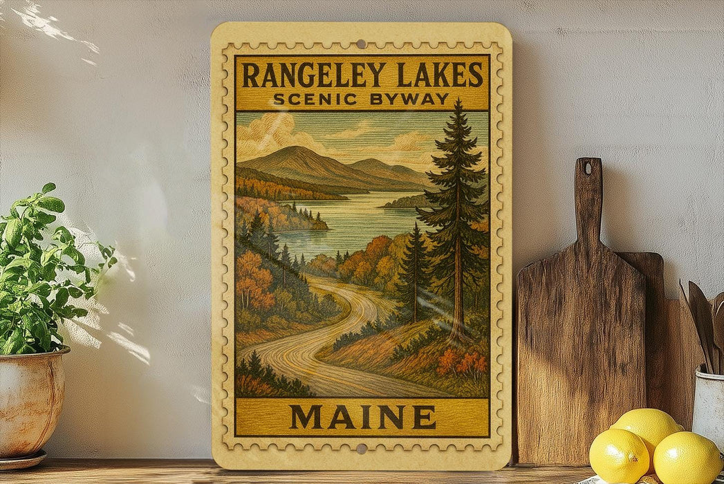 a framed vintage-style illustration of a scenic landscape with a winding road, mountains, and pine trees, along with the text "RANGELEY LAKES SCENIC BYWAY MAINE".