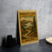 a framed print of a scenic landscape with mountains, trees, and a winding road, depicting the scenic byway of Rangeley Lakes in Maine.