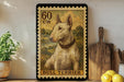 A bull terrier dog is depicted on a framed stamp-like artwork, which is displayed on a shelf next to a wooden cutting board and some lemons.