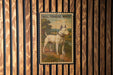 A bull terrier white dog standing on a dirt path in a wooded area, as depicted in a vintage-style metal stamp.