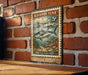 A vintage-style postage stamp featuring a fish, likely a tuna, is displayed on a brick wall.