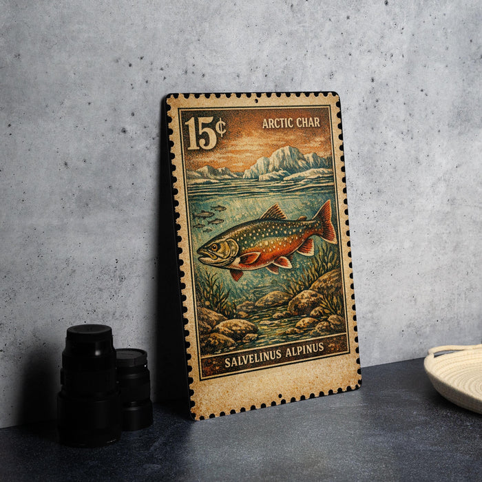 A 15 cent postage stamp from the Arctic Char, featuring an illustration of a salvelinus alpinus fish, is displayed on a gray surface next to some black camera lenses.