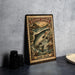 A metal sign with an illustration of a salmon jumping out of the water, surrounded by a river and mountains, is displayed on a table.