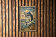 A vintage blue marlin postage stamp is displayed on a wooden wall.