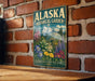 A vintage-style metal sign for the Alaska Botanical Garden, featuring a colorful illustration of various plants and flowers.
