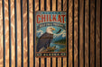 A metal sign with a bald eagle perched on a tree branch, set against a wooden background.