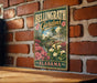 A vintage-style metal sign for Bellingham Gardens in Alabama, featuring a garden scene with pink flowers and a white house.
