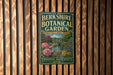 A vintage-style metal sign for the Berkshire Botanical Garden, featuring a garden scene with pink flowers and a bridge in the background.