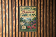 A vintage-style metal sign for the Birmingham Botanical Gardens in Birmingham, Alabama, featuring illustrations of flowers and a building.