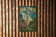 A vintage-style metal sign for the Bok Tower Gardens in Florida, featuring a tropical landscape with palm trees and a tall tower.