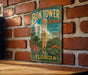 A vintage-style metal sign for the Bok Tower Gardens in Florida, featuring a tropical landscape with a tall tower and lush greenery.