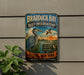 A vintage metal sign for the Braddock Bay Bird Observatory, featuring an illustration of a bird and a bird in flight, with text promoting the observatory and its mission to protect and educate people about the local ecosystem.