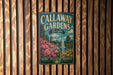A vintage metal sign for Callaway Gardens in Georgia, featuring a scenic landscape with a waterfall and colorful flowers, mounted on a wooden wall.