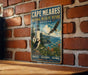 A vintage metal sign for Cape Meares National Wildlife Refuge in Oregon, featuring an illustration of a lighthouse, puffins, and a seagull flying over a coastal landscape.