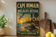 A vintage-style metal sign for Cape Romain National Wildlife Refuge in South Carolina, featuring a seascape with a lighthouse and a bird in flight.