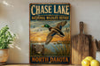 A vintage metal sign for the North Dakota wildlife refuge, featuring a duck in flight against a sunset landscape.
