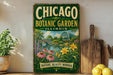 A vintage-style metal sign for the Chicago Botanic Garden in Illinois, featuring a scenic illustration of the garden with flowers, plants, and a bridge.