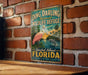 A vintage-style metal sign for the Ding Darling National Wildlife Refuge in Sanibel Island, Florida, featuring a pink flamingo and a dolphin in a tropical setting.