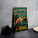 A vintage-style metal sign for Ding Darling National Wildlife Refuge in Sanibel Island, Florida, featuring a pink flamingo and a sunset landscape.