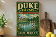 A vintage-style sign for Duke Farms, featuring a scenic landscape with a castle, river, and bird, is displayed on a wooden shelf next to a potted plant and a cutting board.