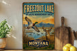 A vintage-style metal sign for Freezout Lake, Montana, featuring an illustration of a bird in flight and a deer in the foreground, with mountains in the background.