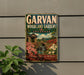 A vintage-style metal sign for the GARVAN Woodland Gardens in Arkansas, featuring a scenic landscape with a bridge, flowers, and a waterfall.