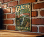 A vintage-style metal sign advertising the Glacier Garden in Montana, featuring a scenic image of a waterfall and a wooden bridge.
