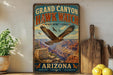 A vintage-style metal sign advertising the Grand Canyon Hawk Watch, featuring an image of a hawk in flight over the Grand Canyon.