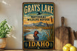 A vintage-style metal sign for the National Wildlife Refuge in Idaho, featuring a duck swimming in a lake and mountains in the background.