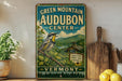 A vintage-style sign for the Green Mountain Audubon Center in Vermont, featuring a colorful illustration of a bird perched on a branch with a scenic landscape in the background.