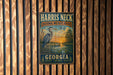 A vintage metal sign for the Harris Neck National Wildlife Refuge in Georgia, featuring a blue heron and a sunset landscape.