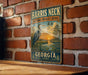 A vintage metal sign for the Harris Neck National Wildlife Refuge in Georgia, featuring an illustration of a heron and a sunset over a body of water.