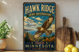 A vintage-style metal sign for Hawk Ridge Bird Observatory in Duluth, Minnesota, featuring an illustration of a hawk in flight against a scenic landscape.