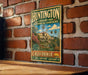 A vintage metal sign for Huntington Library and Botanical Gardens in California, featuring an illustration of a building surrounded by lush greenery.
