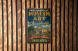 A vintage-style metal sign for the Indianapolis Museum of Art, featuring the museum's name and the words "Art - Nature - Experience - Indiana" in a decorative font.
