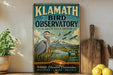 A vintage-style sign for the Klath Bird Observatory in Oregon, featuring an illustration of a heron and birds in flight against a scenic landscape.