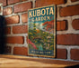 A vintage metal sign for Kubota Garden in Washington, featuring a scenic landscape with a bridge and pagoda.