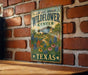 A vintage-style metal sign with the text "LADY BIRD JOHNSON WILDFLOWER CENTER TEXAS" and an illustration of a building surrounded by a garden with colorful flowers.