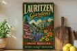 A vintage-style sign for Lauritzen Gardens in Omaha, Nebraska, featuring a colorful illustration of a garden with flowers, a waterfall, and a building.