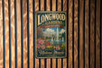 A vintage-style metal sign for Longwood Gardens in Pennsylvania, featuring a fountain and lush greenery, is displayed on a wooden wall.