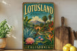 A vintage-style metal sign with a tropical landscape and a pond, featuring the text "LOTUSLAND A Botanical Paradise" and "CALIFORNIA". The sign is displayed on a shelf next to a wooden cutting board and a potted plant.