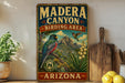 A vintage-style sign for Madera Canyon, Arizona, featuring a colorful illustration of a bird and the text "BIRDING AREA" and "ARIZONA" on a wooden frame.