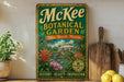 A vintage-style metal sign for the McKee Botanical Garden in Vero Beach, Florida, featuring a tropical garden scene with palm trees, flowers, and a fountain.