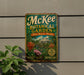 A vintage-style metal sign for the McKee Botanical Garden in Vero Beach, Florida, featuring a tropical garden scene with palm trees, flowers, and a fountain.