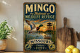 a vintage-style metal sign for the Mingso National Wildlife Refuge in Missouri, with a duck flying over a lake and a sunset in the background.