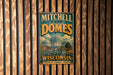 A vintage-style metal sign for Mitchell Park Domes in Milwaukee, Wisconsin, featuring a colorful illustration of the domes and the text "Mitchell Park Domes Milwaukee Wisconsin Discover Explore Inspire".